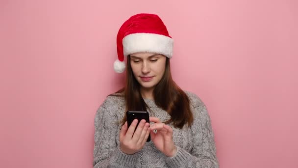 Zszokowana Młoda Kobieta Kapeluszu Santa Christmas Trzymająca Smsy Smartfonie Ubrana — Wideo stockowe