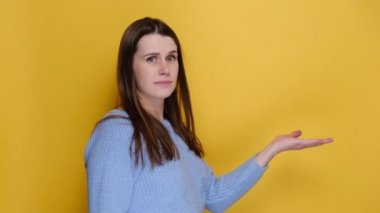 Side profile view of worried irritated disgusted young woman turn around camera spreading hands sweating, dressed in blue sweater, isolated on yellow studio wall. Emotion people lifestyle concept