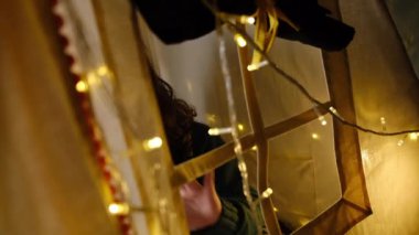 Tatil çelenkleriyle süslü, rahat bir çadırda oturan, evde kış tatili yaparken eğlenen sevimli bir çocuk. Tatlı anların tadını çıkar