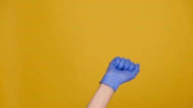 Sayılar hesaplanıyor. 1 'den 5' e kadar parmaklarıyla sayan, tıbbi koruma eldiveni takan, sarı arka planda, reklam için fotokopi alanı olan tanınmamış bir adama yakın çekim. El hareketi