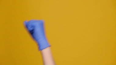 Tıbbi koruma eldivenleriyle yumruk tokalaşan, sarı stüdyo arka planında kopyalanmış, tanınmayan kızgın adamı yakından çek. Tehdit jesti, saldırganlık kavramı, uyarı, ceza