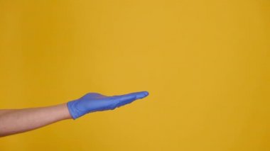 Fotokopi alanındaki avuç içini açıp işaret eden, sarı stüdyo arka planında reklam için izole edilmiş tıbbi koruyucu eldivenler giyen tanınmamış genç bir kadın. Vücut dili kavramı