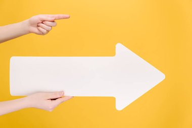 Büyük beyaz kağıt ok tutan kadın ellerini kapat, reklam için fotokopi alanını işaret et, sarı stüdyo arka planında izole edilmiş. Reklam alanı, maket. El hareketi