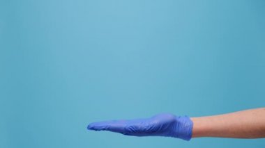 Fotokopi alanındaki avuç içini açıp işaret eden tanınmamış bir genci yakından çek. Reklam için mavi stüdyo arka planında izole edilmiş tıbbi koruyucu eldivenler giy. Vücut dili kavramı