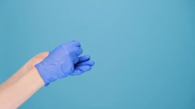 Tanınmayacak kadar genç bir kadın tıbbi koruyucu eldivenleri çıkarıp çöpe atıyor. Reklam için fotokopi çekilen mavi arka planda izole edilmiş. Virüs salgınının sonu kavramı