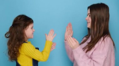 Sevimli anaokulu kızı, mavi arka planda soyutlanmış, tatlı ve genç bir anneyle pasta oynuyor. Mutlu aile annesi ve küçük kız eğlenceli oyunlar öğreniyorlar. Birlikte güzel anların tadını çıkarıyorlar.