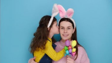 Tatmin olmuş genç bir kadın küçük bir çocuğu taşıyor, pembe tavşan kulakları takıyor. Anne, kızından şok edici mutlu bir hikaye alır. Aile evde Paskalya bayramını kutlar, boyalı yumurtaları tutar, mavi arka planda izole olur.