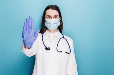 Stetoskop ve beyaz önlüklü ciddi bir kadın doktor, dur işareti, dışarı çıkmanız yasak, mavi arka planda modeller. Covid 19, koronavirüs, sağlık ve doktor konsepti