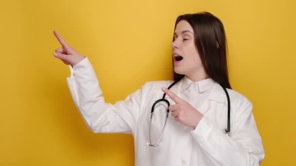黄色の背景に隔離され 興奮し 上の隅を指して見て 興味深い表情で印象的で驚き若い女性医師や看護師 Covid 医療従事者 パンデミックの概念 — ストック動画