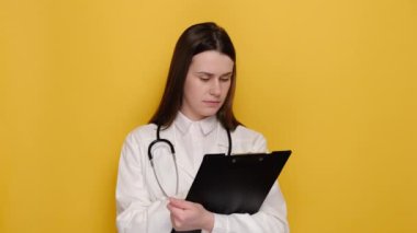 Beyaz önlüklü, sarı arka planda fotokopi çeken, semptomları yazan, kameraya mutlu bakan profesyonel bir kadın doktor. Sağlık çalışanları ve aşı konsepti