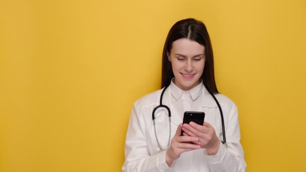 Feliz Joven Médico Vistiendo Abrigo Estetoscopio Usando Teléfono Inteligente Sonriente — Vídeo de stock