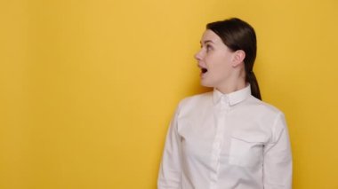 Şaşırmış, neşeli, işaret parmağıyla işaret eden genç bir kadının portresi beyaz gömlek giymiş, sarı stüdyo arka planında fotokopi alanı ile izole edilmiş poz veriyor. İnsanların duygu kavramı