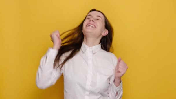 白のシャツを着て 黄色のスタジオの背景に隔離されたポーズをとって はいと言う拳を祝う勝者のジェスチャーを行う幸せな若い女性が興奮しています 業績キャリア富の概念 — ストック動画