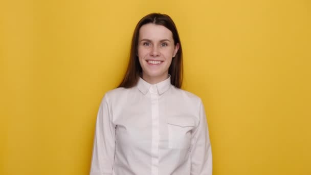 笑顔成功した若いブルネットのビジネス女性の肖像画は 黄色のスタジオの背景に隔離された古典的な白いシャツを着て カメラの点滅ウィンク目を見ている 人々の感情ライフスタイルのコンセプト — ストック動画