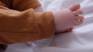 Evdeki rahat beyaz yatakta kahverengi pantolonla uzanan güzel yeni doğmuş bebek bacaklarını kapat. Bebek ayakları küçük, sevimli ve sevimlidir. Seçici odaklanma. Çocukluk kavramı