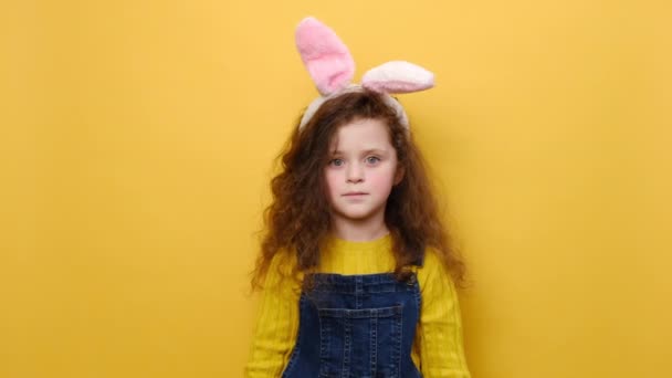 ピンクのウサギのふわふわの耳の肯定的な美しい就学前の女の子は何かのために祈っています コピースペースと黄色のスタジオの背景に隔離されたセーターを着ています イースターの休日と願いのコンセプト — ストック動画
