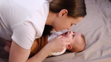 Sevecen, genç, beyaz bir annenin, tatlı, küçük kızıyla evde yatakta geçirdiği şefkatli anların yan görüntüsü. Mutlu anne, gülen küçük bebekle vakit geçiriyor.