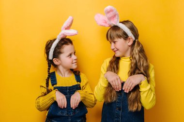 İki terli küçük kız tavşanmış gibi el ele tutuşur, tavşan kulağı takar, birbirlerine bakarlar, sarı arka planda izole bir şekilde gelen Paskalya bayramını kutlamaya hazırdırlar. Bahar tatili kavramı