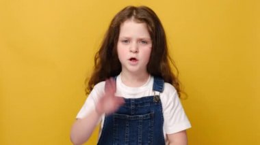 Stüdyonun sarı arka planında izole edilmiş mutsuz küçük bir kız kameraya bak dur işareti yap, mutsuz çocuk reddetme teklifi olmadığını söyle. Sözsüz dil kavramı