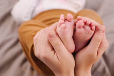 Şefkatli genç anne ellerinin şefkatle bebek ayaklarını tutarken, şefkatle kucağında bebek bacakları tutarken dikkatle baktığı üst manzarayı kapat. Seçici odaklanma. Annelik ve bebek bakımı dışında.