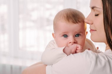 Mutlu bir genç annenin el ele tutuşup küçük tatlı kızına sarılmasının kesilip atılmış görüntüsü sevgi göstergesidir. Gülümseyen anne yeni doğmuş küçük bebeğe sarılıyor. Annelik, çocuk bakımı kavramı.