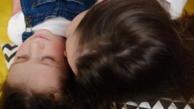 Sevgi dolu genç bir anne evdeki çadırda uzanan küçük tatlı kızını öpüyor. Mutlu, şefkatli bir annenin, anaokulu kızına sarılmasının, sevgi ve şefkat duymasının yan görüntüsü. Annelik kavramı