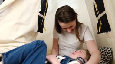 Sevecen genç anne, gülen küçük kızını gıdıklıyor, evde çadırda birlikte rahatlıyor. Mutlu küçük kız eğleniyor, ilgili anne ya da dadıyla oynuyor, hafta sonu eğleniyor.