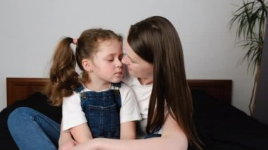 Sevecen anne ve tatlı kızın portresi burunları birbirine değdirip evdeki rahat yatakta oturuyor. Çocuklu ebeveyn eğleniyor. Sevimli küçük çocuk, anneye sevgi göster. Tatlı anın tadını çıkar.