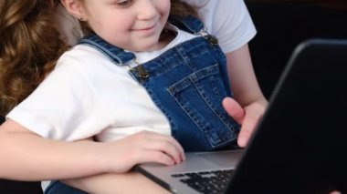Gülümseyen anne ve şirin kız çocuğu internette alışveriş yaparken rahat bir yatakta oturuyor, mutlu anne küçük kıza laptop uygulamasını öğretiyor, çizgi film seyrediyor ya da bilgisayardan video görüşmesi yapıyor.