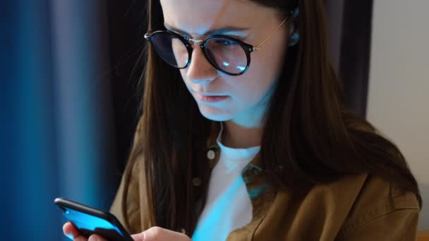 Συγκεντρωμένη Νεαρή Γυναίκα Γυαλιά Χρησιμοποιούν Κινητό Τηλέφωνο Ενώ Βλέποντας Βίντεο — Αρχείο Βίντεο