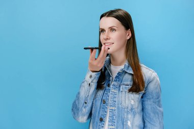 Milenyum kadınlarının elinde telefonla konuşmaları akıllı telefondan sanal dijital ses asistanını aktif hale getiriyor, kız sesli mesaj kaydediyor, arkadaşlarıyla online veya hoparlörden sohbet ediyor, mavi arka planda izole edilmiş.