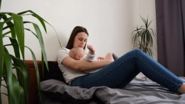 Mutlu bir anne, tatlı bir bebek ve küçük bir kız çocuğu yatakta dinleniyor, anne tatlı kız kardeşlerle eğleniyor, dinleniyor, yatak odasında kestiriyor, aile hafta sonunu birlikte geçiriyor, boş vakitlerin tadını çıkarıyor.