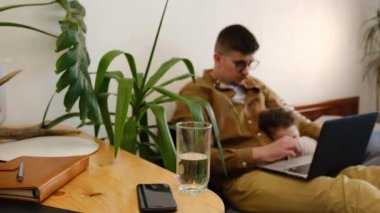 Genç babanın gözlüklü, dizüstü bilgisayarla çalışırken su içtiği seçici odak noktası. Yatakta tatlı küçük bir kızın yanında oturuyor. Babam internet projesinde çalışıyor, iş arkadaşlarıyla iletişim kuruyor ya da internet sörfü yapıyor.
