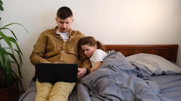 专注的年轻父亲和学龄前孩子坐在床上使用不会说话的电子设备 现代父亲和可爱的小女儿一起工作在小工具上 玩或上网 设备过度使用概念 — 图库视频影像