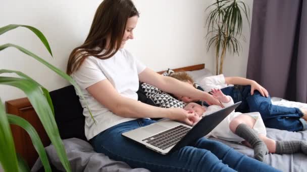 拥有可爱学龄前女儿和婴儿的年轻妈妈在舒适的床上休息 周末在笔记本电脑上看家庭卡通片 享受在家里的闲暇时光 现代技术使用概念 — 图库视频影像