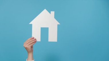 Genç bayanların el kaldırmalarını ve küçük beyaz kağıt evi göstermelerini, reklam için fotokopi alanı olan mavi arka plan duvarında izole edilmiş poz vermelerini. Mülkiyet ve ipotek kavramı