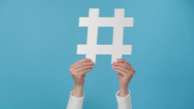Büyük beyaz hashtag işareti, viral web içeriği, internet promosyonu, mavi stüdyo arka plan duvarı üzerinde izole edilmiş kadın ellerine yakın çekim. Moda sosyal medya gönderileri ve blog yazma kavramı