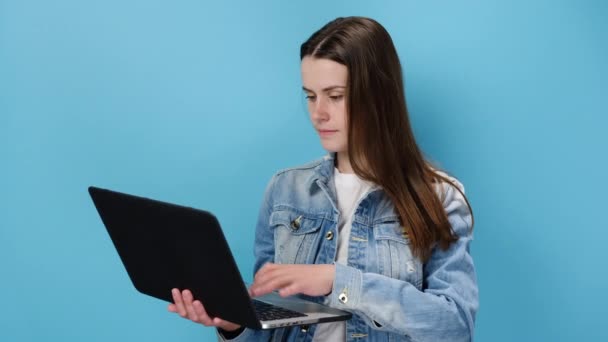 美しい若い正の白人女性20代は ノートパソコンを使用して手に持っているジェスチャーのような親指を表示 カメラで幸せな場所 デニムジャケットに身を包んだ 青いスタジオの背景に隔離された — ストック動画