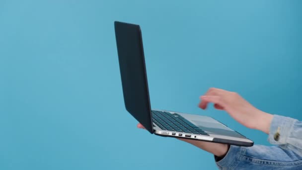 キーボードで入力し コピースペースの青い壁に隔離された承認または合意のサインとして親指を表示するノートパソコンで作業を保持する女性の手のクロップ 広告ワークスペースのモックアップ — ストック動画