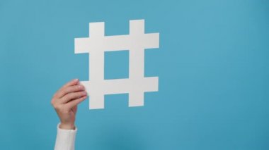 Kadın eli büyük beyaz hashtag işareti taşıyor ve tamam jesti gösteriyor, viral web içeriği, internet tanıtımı, mavi stüdyo arka plan duvarı üzerinde izole edilmiş. Blog günlüğü web sitesi stratejisi kavramı
