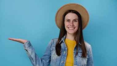 Heyecanlı, genç ve güzel bir bayanın işaret parmağı boş avucunun üzerinde. Vay canına, başparmağını jest gibi gösteriyor. Kot ceket ve şapka giymiş, mavi stüdyo arka planında mankenler var. Halk yaşam tarzı konsepti