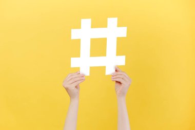 Büyük beyaz hashtag işareti, viral web içeriği, internet promosyonu, sarı arka plan duvarında izole edilmiş kadın eli resimleri. Moda sosyal medya gönderileri ve blog yazma kavramı