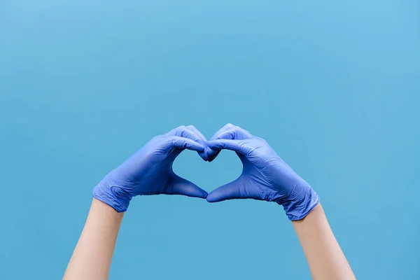 Close up of male hands in medical protection gloves making heart symbol as a way to show thank gratitude to doctors and nurses for help in fight against disease, isolated on blue background. COVID 19