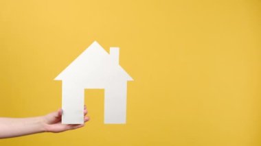 Emlak konsepti. Beyaz kağıt minyatür evi tutan kadınların ellerini kapatın ve iyi değerlendirmeler yapın, sarı arka planda reklam için kopya alanı bulundurun.