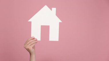 Kadın eller kağıt ev modelini tutuyor ve iyi bir jest yapıyor, emlak evi onayı, pembe stüdyo arka planında izole edilmiş, reklam için fotokopi alanı var. Ev ile ilgili sosyal hizmet kavramı