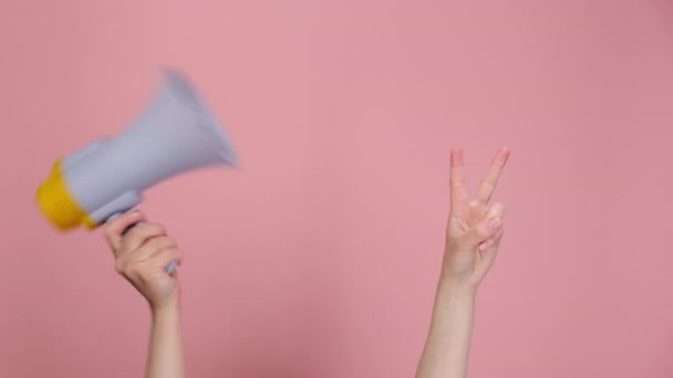 メガホンを持っている女性の手は平和の印はピンクの背景に隔離されたあなたの広告内容のための歓迎ジェスチャーコピースペースを示す2本の指を保つ作る 勝利のお祝いと勝利のコンセプト — ストック動画