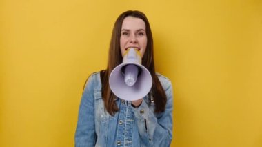 Şok olmuş genç bir kızın portresi megafonla bağırıyor, parmaklarını sana doğru uzatıyor, kot ceket giymiş, sarı arka plan duvarına izole bir şekilde poz veriyor. İnsanlar duygusal yaşam tarzı konsepti