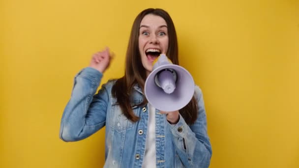 兴奋的年轻的欧洲女人20岁的尖叫在扩音器指向食指旁边 穿着蓝色斜纹棉布夹克 摆出孤立的黄色工作室背景 人的生活方式概念 — 图库视频影像