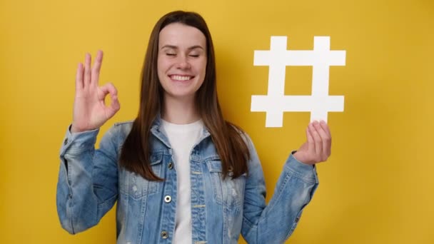 大きなハッシュタグのサインを保持し 黄色のスタジオの背景に隔離された正しいジェスチャー ウイルスのウェブコンテンツ インターネットプロモーションを示す幸せな笑顔の若い女性 ブログ ウェブサイト戦略コンセプト — ストック動画