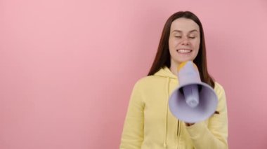 Megafonla bağıran genç bir kadın büyük bir etiket işareti gösteriyor, sarı kapüşonlu giyiyor, pembe arka planda izole edilmiş. Pazarlama ağı, SMM işi, müşteri eğlencesi kampanyası konsepti